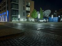 a street corner in the evening with a city building lit up and a street light that is shining blue