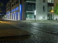 a street corner in the evening with a city building lit up and a street light that is shining blue