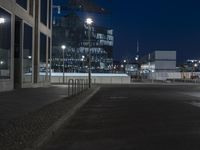 an empty street with some parked motorcycles in the distance at night, in front of a modern building