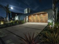 the large concrete home has a wooden garage and several planters around it at night