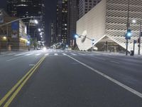 an empty empty street with some lights on at night in front of a modern structure