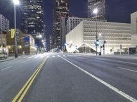 an empty empty street with some lights on at night in front of a modern structure