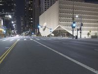 an empty empty street with some lights on at night in front of a modern structure