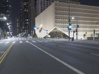 an empty empty street with some lights on at night in front of a modern structure