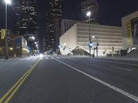 an empty empty street with some lights on at night in front of a modern structure