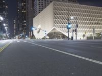 an empty empty street with some lights on at night in front of a modern structure