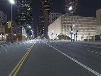 an empty empty street with some lights on at night in front of a modern structure