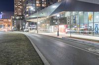 the view of a city from across the street at night showing buildings and a bus stop