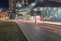 the view of a city from across the street at night showing buildings and a bus stop