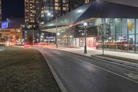 the view of a city from across the street at night showing buildings and a bus stop