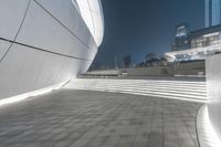 a concrete walkway with a white wall that has lights on it and in the distance is many buildings