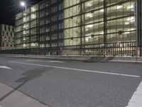 an empty street with some buildings in the background at night time, which appears to be a glass office building