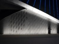 a white building sitting under blue lights near a parking lot on the street at night