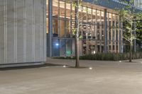 the entrance to a large building on the sidewalk is lit up at night as the lights shine