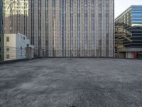 a large building in an empty lot with some buildings behind it and sky scrapes