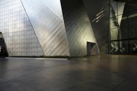 large stainless building next to other buildings in an open space with lots of windows and lighting