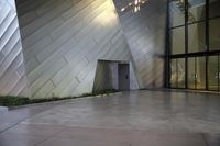 large stainless building next to other buildings in an open space with lots of windows and lighting
