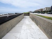 a view of a concrete walkway next to a sea shore and a city street with many buildings