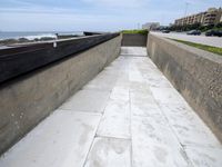 a view of a concrete walkway next to a sea shore and a city street with many buildings