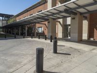 a concrete walkway with black pillars and poles in front of an office building, with a white awning