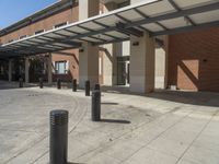 a concrete walkway with black pillars and poles in front of an office building, with a white awning