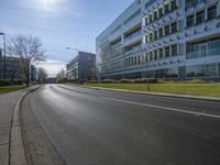 empty road with cars driving past building and trees in the background while sun shines down