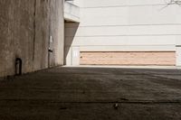 skateboarder standing on cement with buildings in background with sunlight on ground below wall