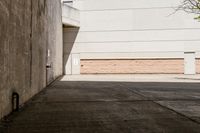 skateboarder standing on cement with buildings in background with sunlight on ground below wall