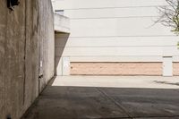 skateboarder standing on cement with buildings in background with sunlight on ground below wall