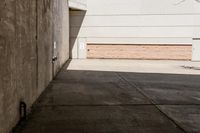 skateboarder standing on cement with buildings in background with sunlight on ground below wall