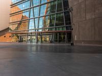 a sidewalk outside some very tall building with glass walls and floors, there is a bench near the walkway