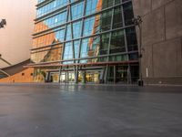 a sidewalk outside some very tall building with glass walls and floors, there is a bench near the walkway