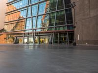 a sidewalk outside some very tall building with glass walls and floors, there is a bench near the walkway