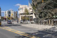 two people on a bicycle and a car driving down the street by tall buildings on a clear day