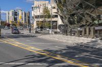 two people on a bicycle and a car driving down the street by tall buildings on a clear day