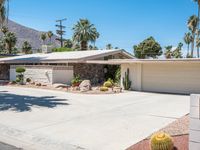 a house with desert landscaping in the front and a cacti plant and rock on the sidewalk