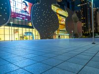 night scene with large building near sidewalk, glass facade and street lights in background and buildings on other side