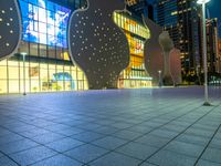 night scene with large building near sidewalk, glass facade and street lights in background and buildings on other side