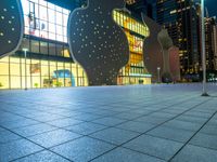 night scene with large building near sidewalk, glass facade and street lights in background and buildings on other side