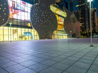 night scene with large building near sidewalk, glass facade and street lights in background and buildings on other side