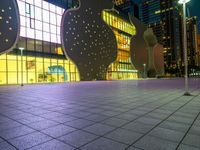 night scene with large building near sidewalk, glass facade and street lights in background and buildings on other side