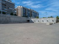 the empty parking lot in front of a wall with apartment buildings on it and a skateboarder on a ramp