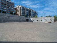 the empty parking lot in front of a wall with apartment buildings on it and a skateboarder on a ramp