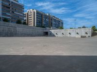 the empty parking lot in front of a wall with apartment buildings on it and a skateboarder on a ramp