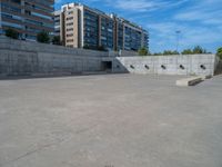 the empty parking lot in front of a wall with apartment buildings on it and a skateboarder on a ramp