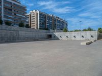 the empty parking lot in front of a wall with apartment buildings on it and a skateboarder on a ramp