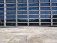 a cement floor in front of an industrial glass building with some windows behind it in a flat light