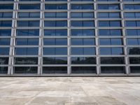 a cement floor in front of an industrial glass building with some windows behind it in a flat light