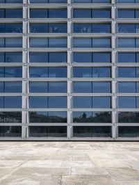 a cement floor in front of an industrial glass building with some windows behind it in a flat light