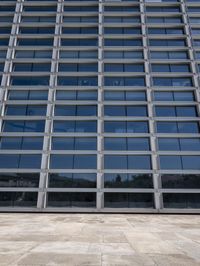 a cement floor in front of an industrial glass building with some windows behind it in a flat light